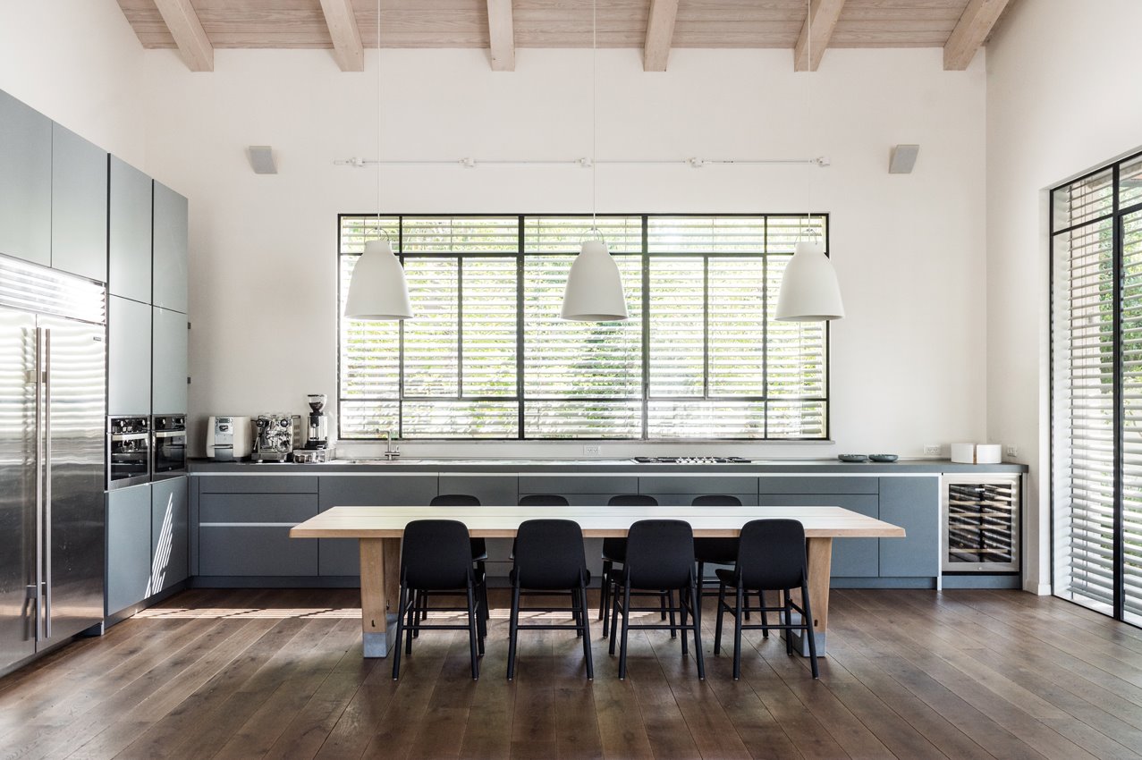 המטבח: שולחן עץ גדול שניצב במרכז שטחו משתלב עם עיצוב מודרני-נקי.  שלושה גופי תאורה גדולים המשתלשלים מעליו, מדגישים את נוכחותו. צילום: גלעד רדט